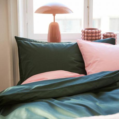 Ropa de cama verde oscuro con fundas de almohada rosas.
