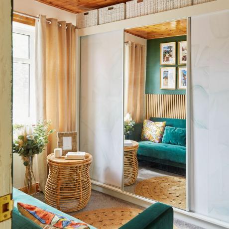 Свободная комната с зеленым диваном и шкафом для хранения вещей с зеркалом в полный рост.
