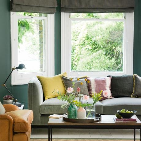 Dzīvojamā istaba ar tumšiem dīvāniem un krāsotiem logu rāmjiem