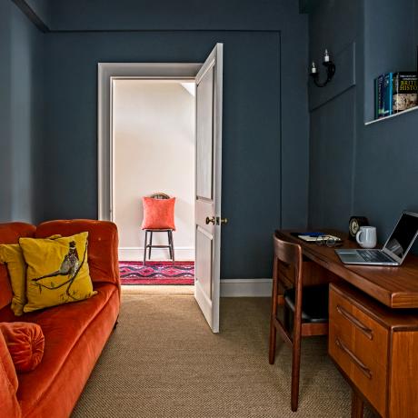 mali kućni ured sa tamno obojenim zidovima i sofom od narančaste sofe