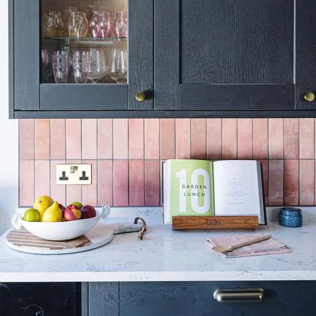 schwarze Küchenschränke mit rosa Fliesen und weißer Arbeitsplatte
