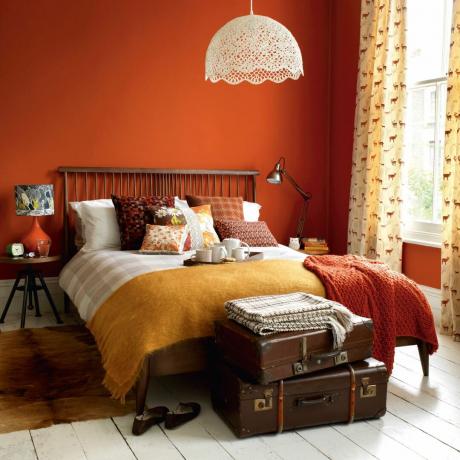 oranžinis miegamasis su sluoksniuotomis pagalvėlėmis ir raštuotomis užuolaidomis