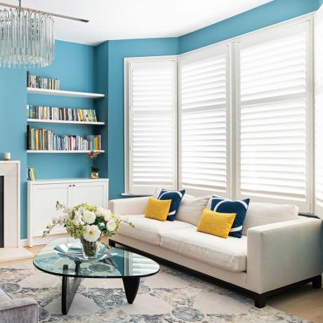 Blå stue med bogreoler, pejs, lysekrone og creme sofa foran spejlet