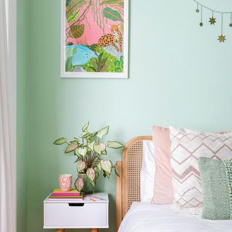 Zelená ložnice s růžovým povlečením a bílým nočním stolkem