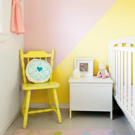 Bērnistaba ar bērnu gultiņu, dzeltenu krēslu un dzelteni rozā krāsotām sienām