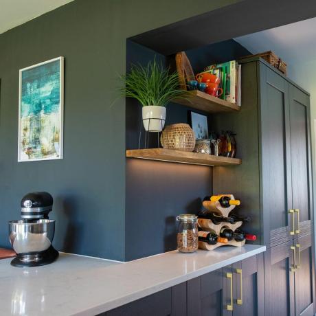 خزانة مطبخ زرقاء وشبه جزيرة مع سطح عمل رخامي ورفوف فوقها