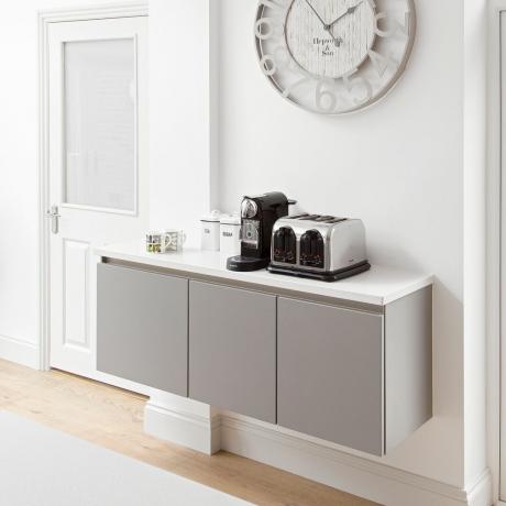Sett med elegante grå vegghengte enheter i en hvit plass satt opp for å holde kaffemaskin, krus og kaffetilbehør