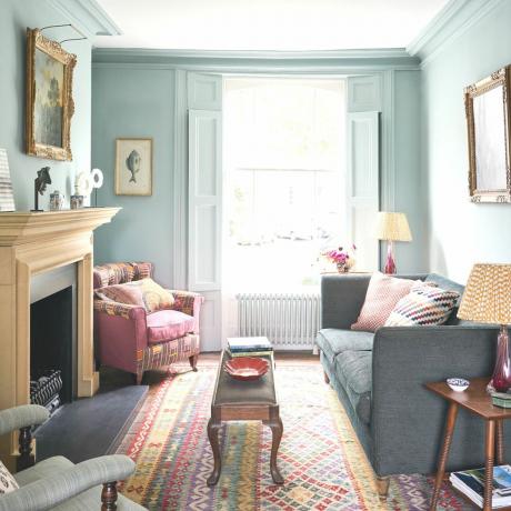 niebieski salon z różowym krzesłem i szarą sofą naprzeciwko drewnianego kominka