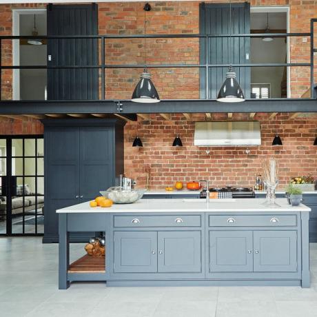 Virtuvė su atviromis plytų sienomis, pilka spintele ir antresoliniu koridoriumi