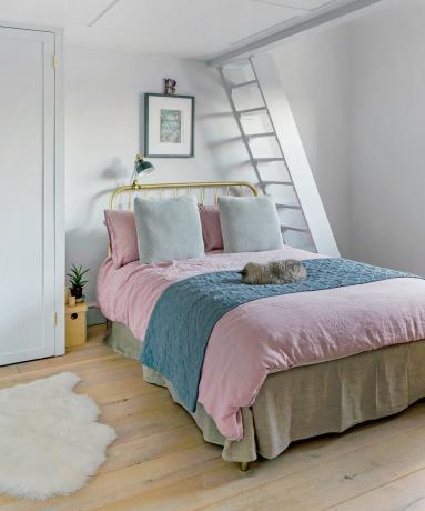 Vitt sovrum med rosa sängkläder och stege till vinden