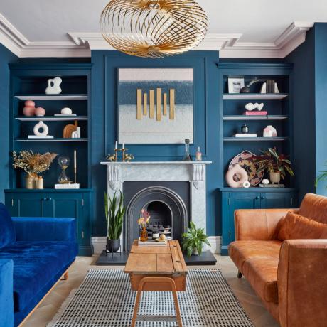 Stue med mørkeblå malte vegger, en blå sofa og en brunfarget skinn