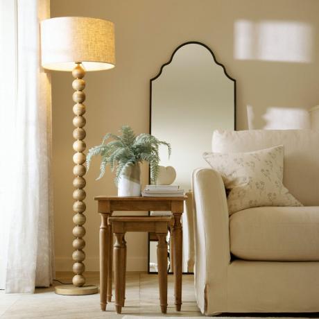 neutrální obývací pokoj s pohovkou a dřevěnou stojací lampou s bambulí a neutrálním bubnovým stínidlem