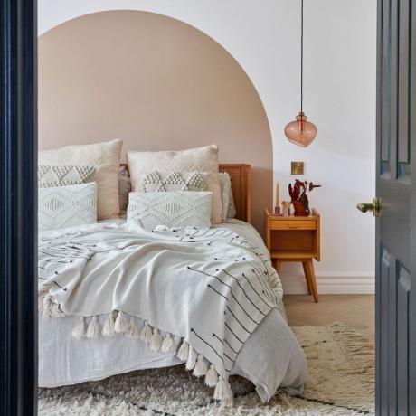 Sovrum med välvd målareffekt bakom sängen och strökuddar på sängen