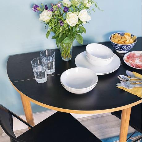 blå vägg med svart drop leaf bord och vitt porslin och glas