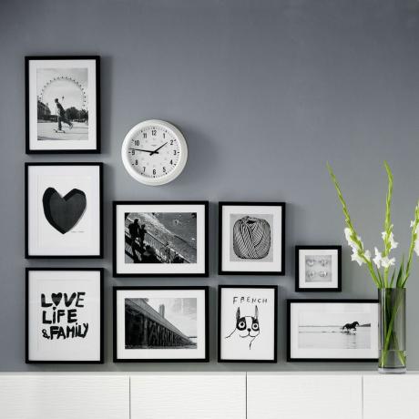 Middengrijze wand met L-vormige gallery wall of art in zwarte lijsten met daaronder een wit dressoir
