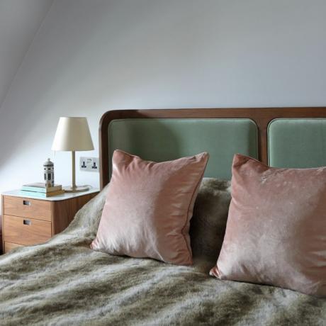 Neitrāla rozā un zaļa gulta guļamistabā ar baltām sienām