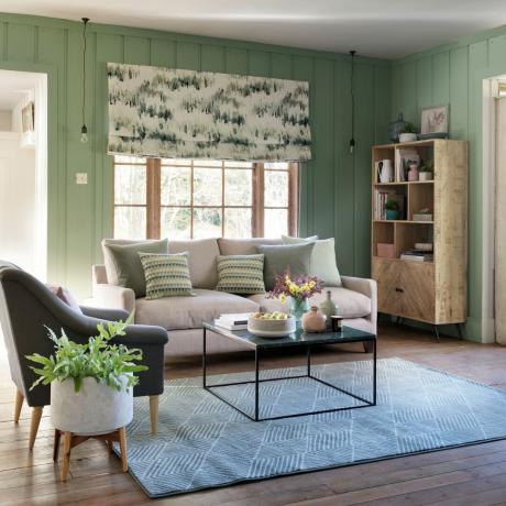 Ruang tamu hijau dengan panel dinding, lantai kayu, dan permadani abu-abu