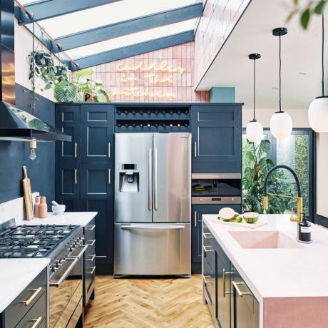 frigider argintiu în dulapuri albastre cu luminator, insulă de bucătărie cu blaturi roz și podea din lemn