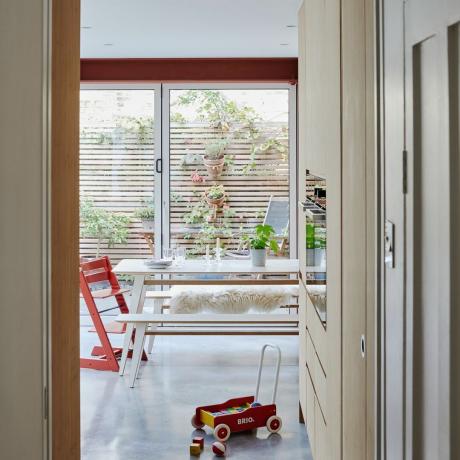 pemandangan dari lorong ke ruang makan dapur keluarga dengan meja makan, kursi tinggi Tripp Trapp, mobil mainan, dan pintu bifold