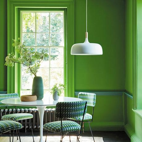 Rohkean vihreä ruokasali, jossa on valkoinen jalustallinen ruokapöytä ja riippuvalaisin