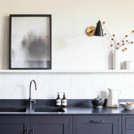 virtuvė su juodu stalviršiu ir balta siena su lentyna ir sieniniu šviestuvu