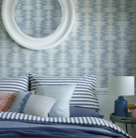 Blå soveværelse med stribet sengetøj og mønstret tapet