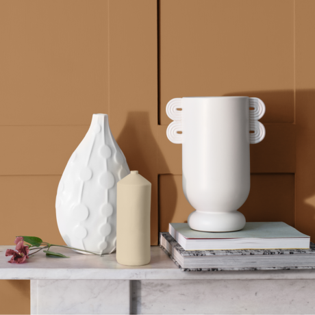 Subtil gullfarget malt vegg med peishylle i hvit marmor med hvit keramikk og stearinlys