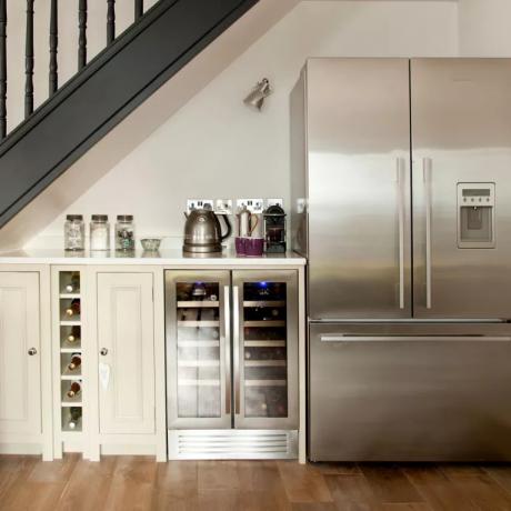 Ein Weinkühlschrank und ein freistehender Kühlschrank mit Gefrierfach entlang einer Wand unter der Treppe