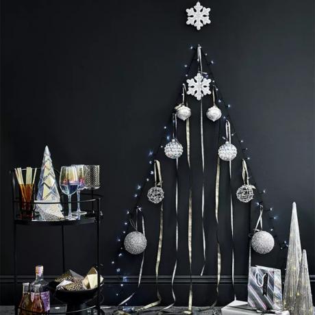 Alternatyvios Kalėdų eglutės su niekučiais ant juodos sienos