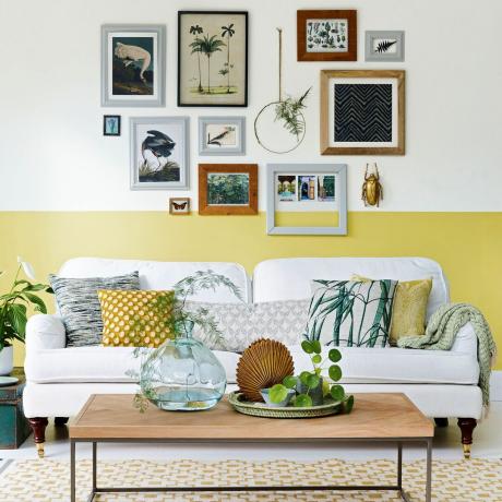 Jasny salon z częściowo pomalowaną na żółto ścianą i organicznym układem ścian z obrazami