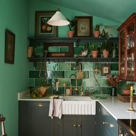 grüne Küche mit großen Fliesen, offenen Regalen und Kunstwerken