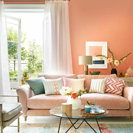 Roosade seinte, valge põranda ja kardinatega elutuba, aeda avanevad prantsuse aknad ning pastelsetes, roosades ja kollastes toonides mööbel ja kaunistused
