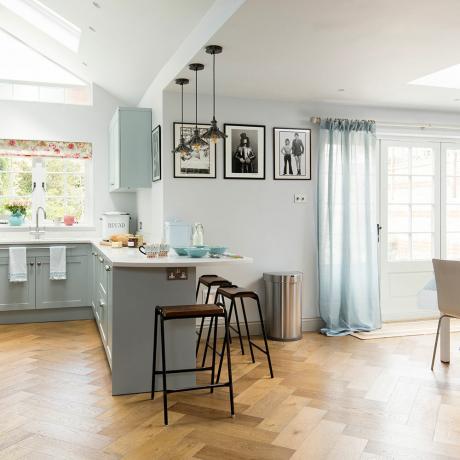 Virtuvės virtuvės perdarymas su šviesiai mėlynomis spintelėmis, žibintu ant stogo ir parketo grindimis