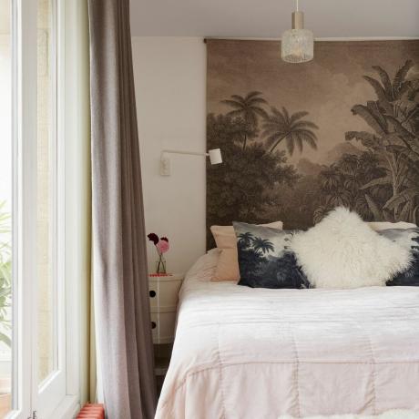 Sypialnia z gobelinem w kształcie palmy wiszącym nad łóżkiem, jasnoróżową pościelą i akcentującymi poduszkami