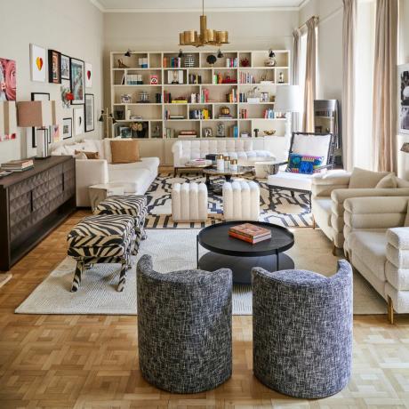 Nøytral tonet stue med sofa, lenestoler og en bokhylle-aksentvegg
