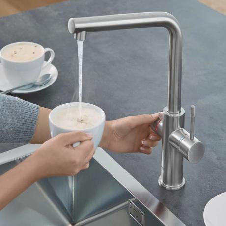 一杯のコーヒーに水を加えるために使用される銀色の熱湯蛇口