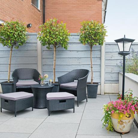 Große Terrasse mit Sitzbereich neben einem grau gestrichenen Zaun mit Lorbeerbäumen