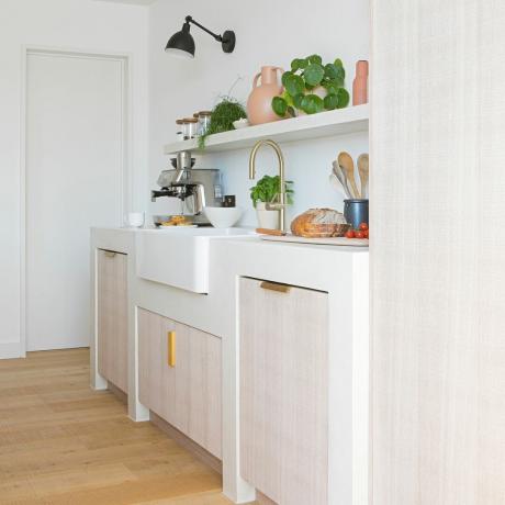 Una cocina con fregadero de mayordomo blanco, cafetera de acero inoxidable, grifo de latón y estantería blanca