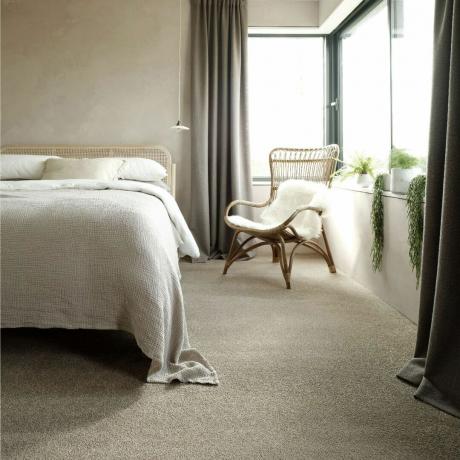 neutralt sovrum med blek neutral matta, beiga väggar och en flätad stol och sänggavel