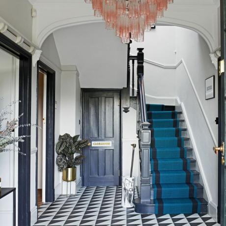 corredor com piso monocromático, escada com corredor azul e lustre rosa