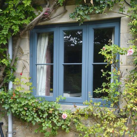 Fenêtres traditionnelles fenêtres en accoya bleu dans un bâtiment en pierre avec des rosiers grimpants et des glycines