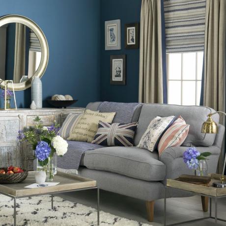 mėlyna svetainė su pilka sofa ir veidrodžiu