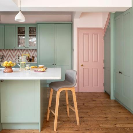 Kjøkken med lysgrønne enheter i full høyde og en rosa dør