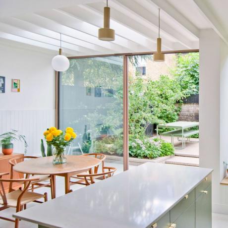 кухненска трапезария със сканди маса и столове големи отворени врати във вътрешния двор и жълти цветя във ваза