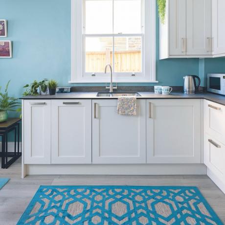Белая кухня с окрашенными в синий цвет стенами и соответствующим синим ковриком.