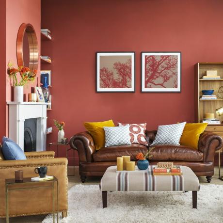 Гостиная в землисто-красном цвете с насыщенным коричневым кожаным диваном в стиле Честерфилд и мягкой подставкой для ног.