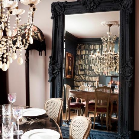 غرفة طعام بها مرآة بطول الأرضية وثريا فوق طاولة طعام مستديرة بها كؤوس وأطباق وأدوات مائدة في منزل مستقل على الطراز الجورجي. منزل لويز وستيوارت براون في تونبريدج ويلز، كينت.