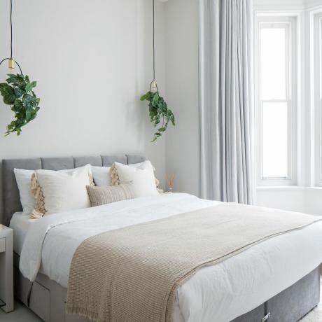 חדר שינה לבן עם מיטה זוגית וצמחים תלויים משני הצדדים