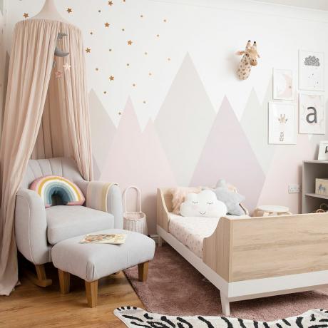 Otroška spalnica s pastelno roza gorami, stolom za dojenje in baldahinom