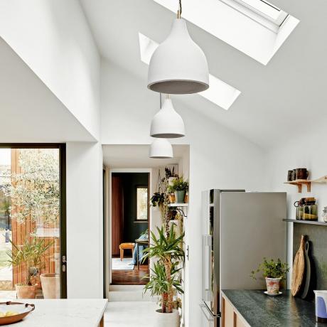 Biela moderná otvorená kuchyňa so strešnými oknami a závesnými svietidlami